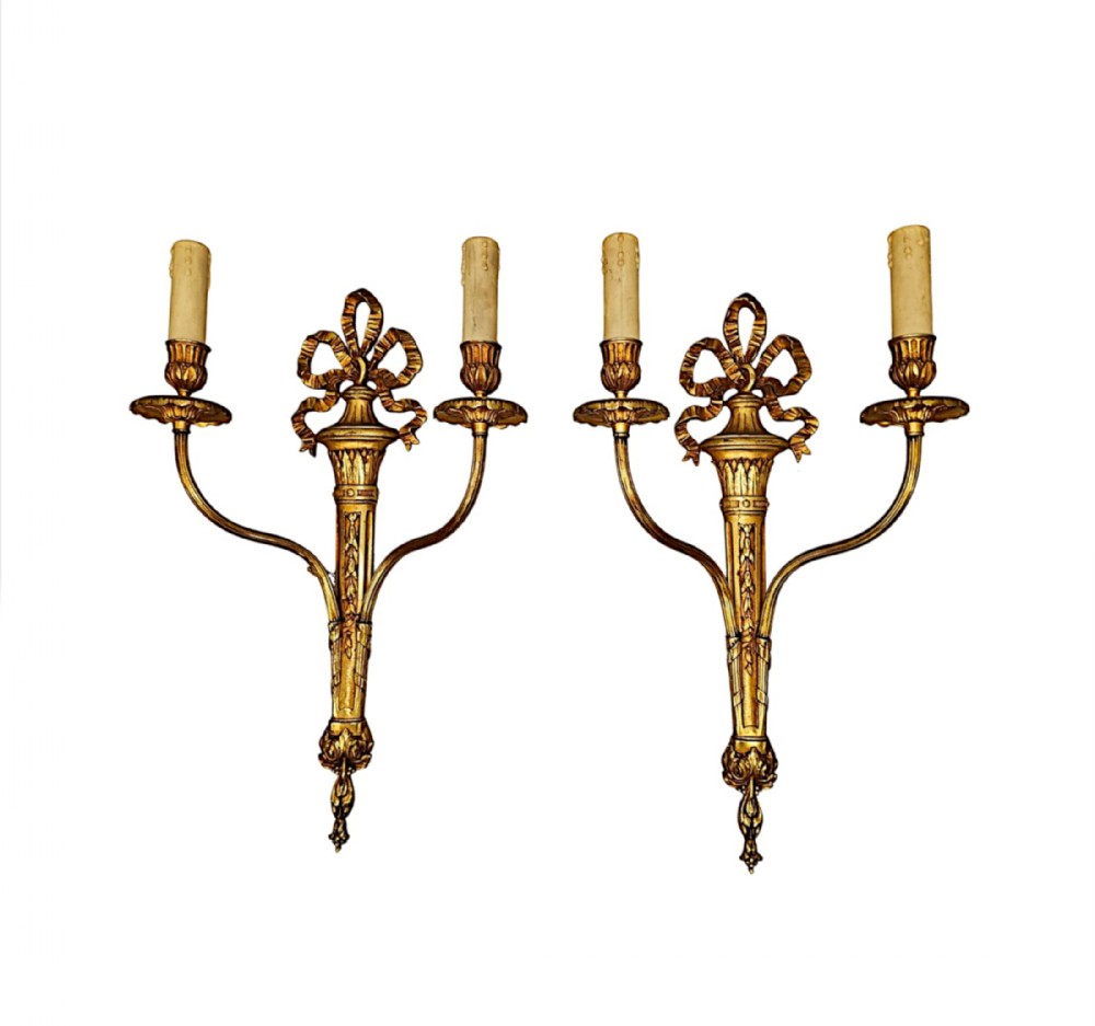 A pair of early twentieth-century Louis XVI style gilt bronze twin-arm wall sconces decorated with ribbon bows and floral motifs.