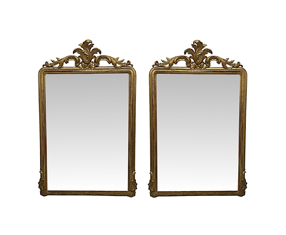 A pair of tall 19th-century giltwood rectangular overmantel mirrors featuring ornate carved acanthus leaf cresting and beaded inner borders.