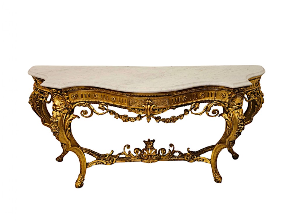 A late 18th-century giltwood console table featuring a serpentine white marble top, elaborate carved scrollwork legs, and floral swags.