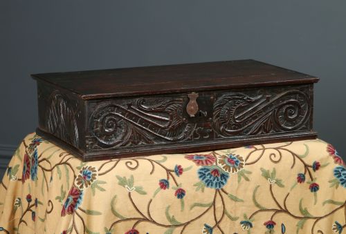 fig 1. A dark brown 17th-century carved oak bible box featuring intricate scrollwork on the front panel and a central iron keyhole escutcheon.