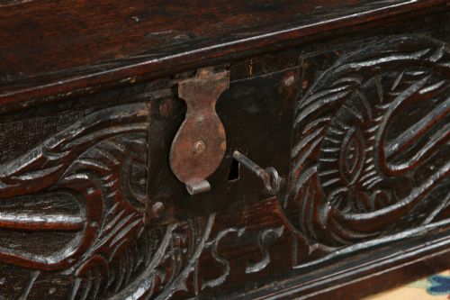fig 3. A dark brown 17th-century carved oak bible box featuring intricate scrollwork on the front panel and a central iron keyhole escutcheon.
