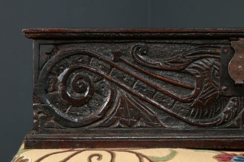 fig 4. A dark brown 17th-century carved oak bible box featuring intricate scrollwork on the front panel and a central iron keyhole escutcheon.