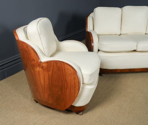 fig 1. An antique Art Deco three-piece lounge suite consisting of a three-seater sofa and two matching armchairs upholstered in cream leather with curved walnut side panels.