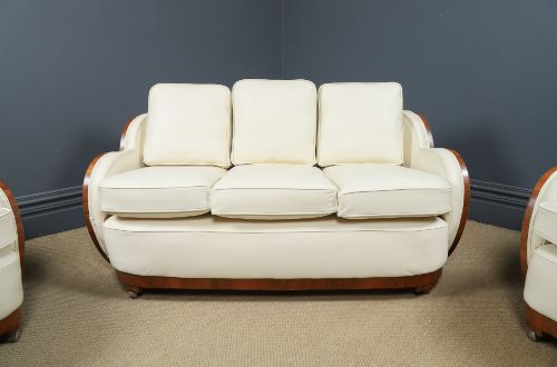 fig 4. An antique Art Deco three-piece lounge suite consisting of a three-seater sofa and two matching armchairs upholstered in cream leather with curved walnut side panels.