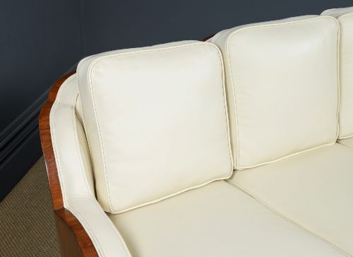 fig 5. An antique Art Deco three-piece lounge suite consisting of a three-seater sofa and two matching armchairs upholstered in cream leather with curved walnut side panels.