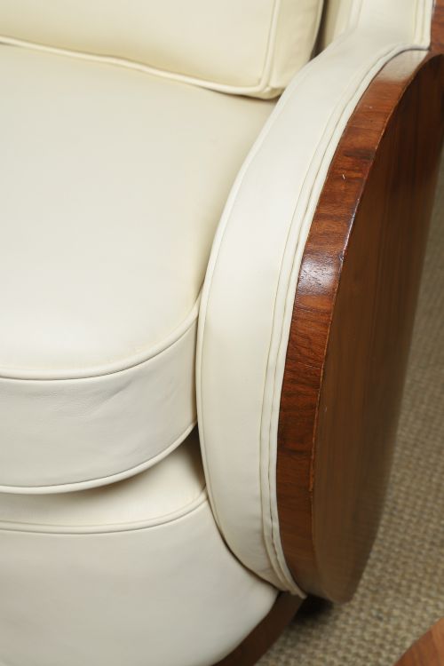 An antique Art Deco three-piece lounge suite consisting of a three-seater sofa and two matching armchairs upholstered in cream leather with curved walnut side panels. View VIII