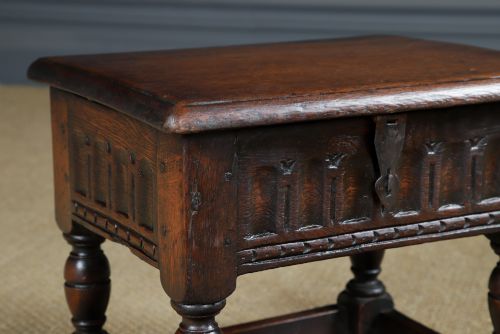 fig 2. A small antique dark oak box stool featuring a hinged top lid, hand-carved frieze panels, turned legs, and square perimeter stretchers.