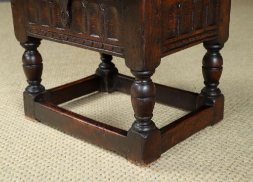 fig 5. A small antique dark oak box stool featuring a hinged top lid, hand-carved frieze panels, turned legs, and square perimeter stretchers.