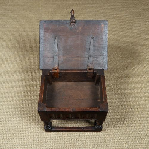 fig 6. A small antique dark oak box stool featuring a hinged top lid, hand-carved frieze panels, turned legs, and square perimeter stretchers.