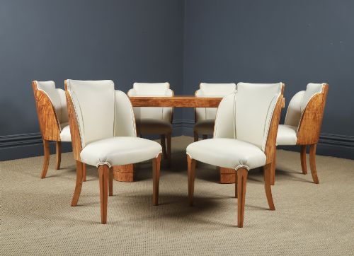 fig 1. An English Art Deco dining suite featuring a rectangular satinwood and maple dining table with a glass top and six cream leather upholstered chairs with curved veneered backs.