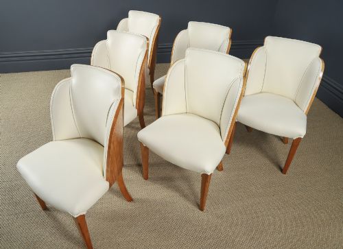 fig 2. An English Art Deco dining suite featuring a rectangular satinwood and maple dining table with a glass top and six cream leather upholstered chairs with curved veneered backs.