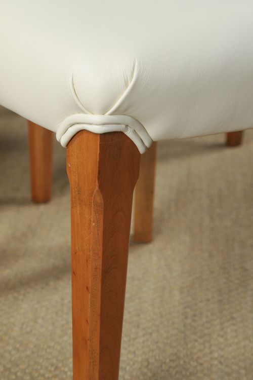 fig 4. An English Art Deco dining suite featuring a rectangular satinwood and maple dining table with a glass top and six cream leather upholstered chairs with curved veneered backs.