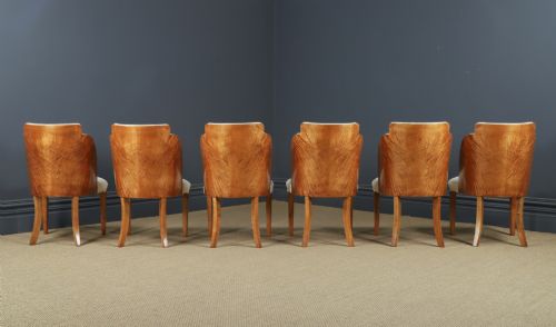 fig 5. An English Art Deco dining suite featuring a rectangular satinwood and maple dining table with a glass top and six cream leather upholstered chairs with curved veneered backs.