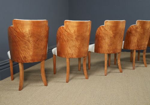 fig 6. An English Art Deco dining suite featuring a rectangular satinwood and maple dining table with a glass top and six cream leather upholstered chairs with curved veneered backs.