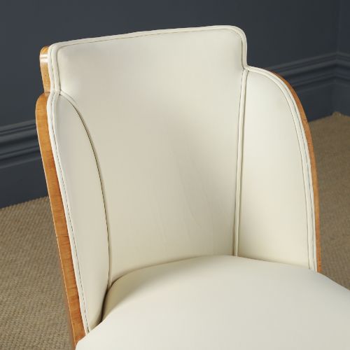 fig 8. An English Art Deco dining suite featuring a rectangular satinwood and maple dining table with a glass top and six cream leather upholstered chairs with curved veneered backs.