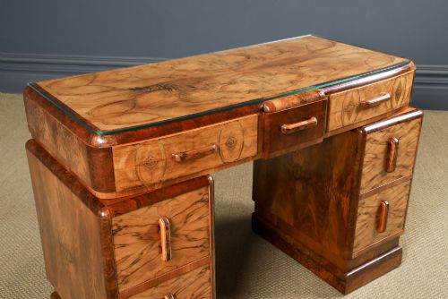 fig 1. An Art Deco walnut and burr elm pedestal desk featuring stepped side pedestals, bookmatched wood veneers, wooden handles, and a fitted glass top.