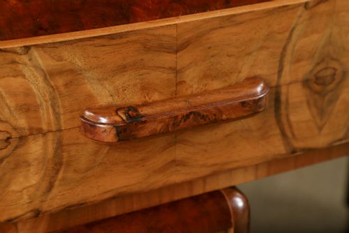 fig 4. An Art Deco walnut and burr elm pedestal desk featuring stepped side pedestals, bookmatched wood veneers, wooden handles, and a fitted glass top.