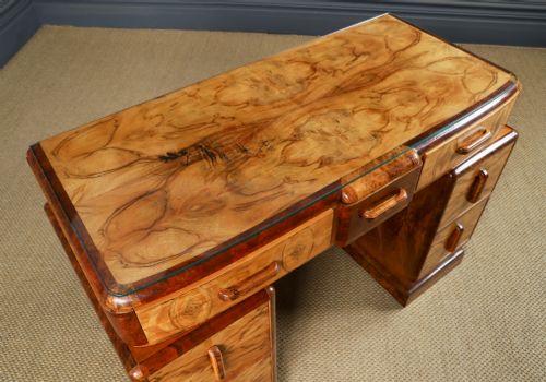 fig 6. An Art Deco walnut and burr elm pedestal desk featuring stepped side pedestals, bookmatched wood veneers, wooden handles, and a fitted glass top.