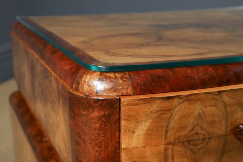 fig 7. An Art Deco walnut and burr elm pedestal desk featuring stepped side pedestals, bookmatched wood veneers, wooden handles, and a fitted glass top.