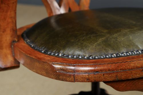 fig 6. An Edwardian oak revolving desk armchair featuring a carved pierced back splat, green leather upholstered seat with close studding, and a four-point swivel base on brass castors.