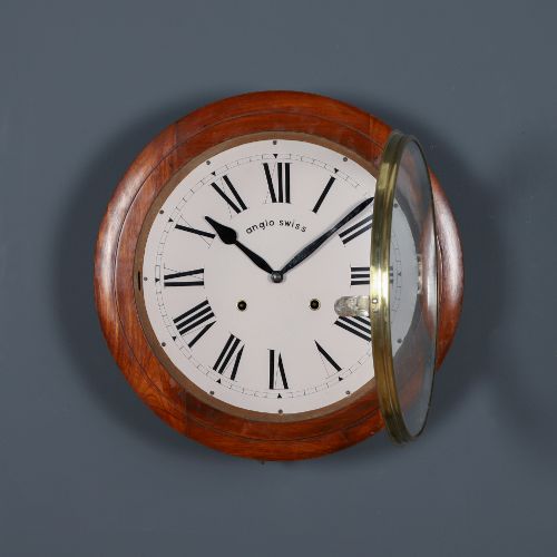 fig 1. A circular antique wall clock featuring a turned mahogany frame, brass bezel, and white dial with black Roman numerals marked Anglo Swiss.