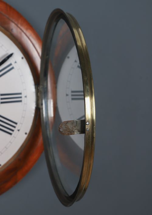 fig 3. A circular antique wall clock featuring a turned mahogany frame, brass bezel, and white dial with black Roman numerals marked Anglo Swiss.