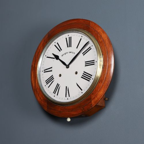 fig 7. A circular antique wall clock featuring a turned mahogany frame, brass bezel, and white dial with black Roman numerals marked Anglo Swiss.