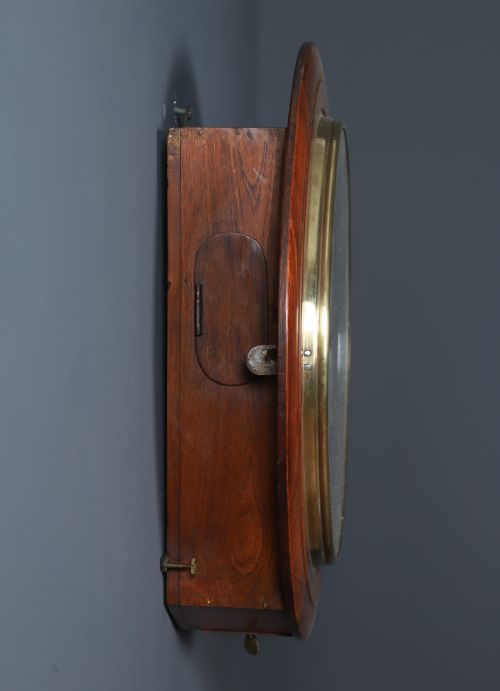 fig 8. A circular antique wall clock featuring a turned mahogany frame, brass bezel, and white dial with black Roman numerals marked Anglo Swiss.