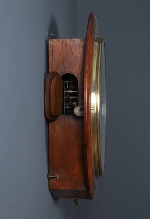 fig 9. A circular antique wall clock featuring a turned mahogany frame, brass bezel, and white dial with black Roman numerals marked Anglo Swiss.