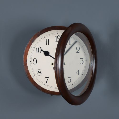 fig 1. A circular mahogany wall clock with a cream dial, black Arabic numerals, black metal hands, two brass winding holes, and the Enfield maker name printed in the centre.