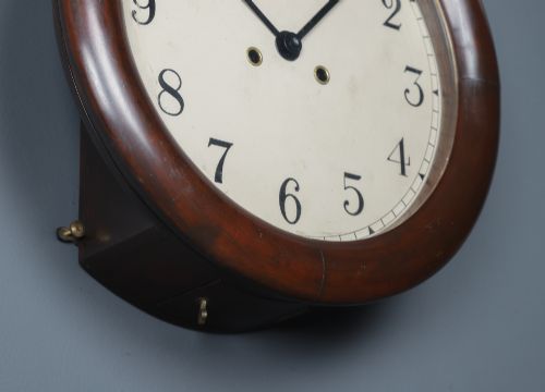 fig 4. A circular mahogany wall clock with a cream dial, black Arabic numerals, black metal hands, two brass winding holes, and the Enfield maker name printed in the centre.