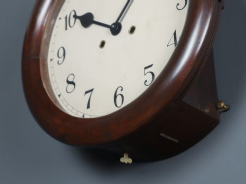 fig 6. A circular mahogany wall clock with a cream dial, black Arabic numerals, black metal hands, two brass winding holes, and the Enfield maker name printed in the centre.