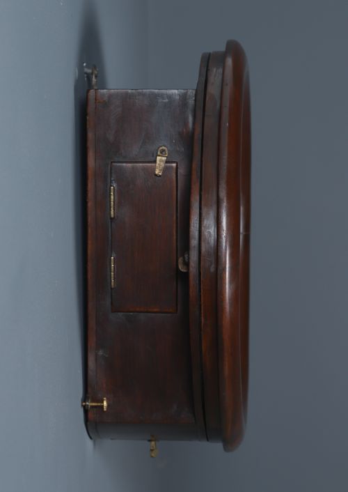 fig 8. A circular mahogany wall clock with a cream dial, black Arabic numerals, black metal hands, two brass winding holes, and the Enfield maker name printed in the centre.
