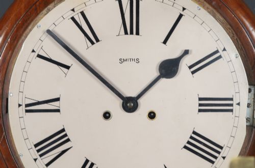 fig 2. A circular Smiths antique wall clock with a turned mahogany wood surround, off-white dial with black Roman numerals, brass hinged bezel, and winding holes.