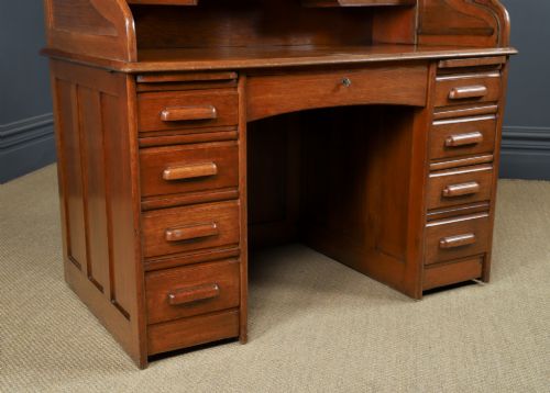 fig 1. An Edwardian warm brown oak twin-pedestal rolltop desk featuring a flexible slatted wooden tambour shutter open to reveal internal pigeonholes above nine drawers with wooden cup handles.