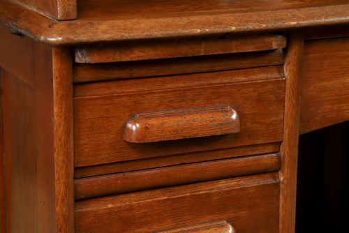 fig 2. An Edwardian warm brown oak twin-pedestal rolltop desk featuring a flexible slatted wooden tambour shutter open to reveal internal pigeonholes above nine drawers with wooden cup handles.