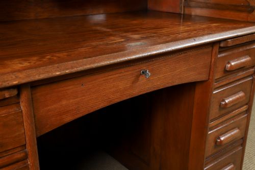 fig 3. An Edwardian warm brown oak twin-pedestal rolltop desk featuring a flexible slatted wooden tambour shutter open to reveal internal pigeonholes above nine drawers with wooden cup handles.
