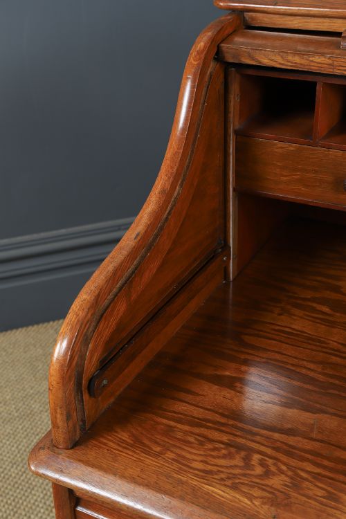 fig 7. An Edwardian warm brown oak twin-pedestal rolltop desk featuring a flexible slatted wooden tambour shutter open to reveal internal pigeonholes above nine drawers with wooden cup handles.