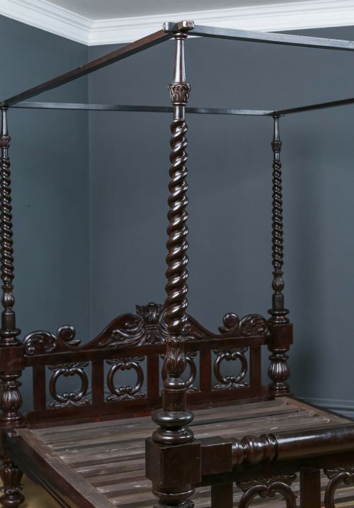 fig 4. An antique dark timber king-size four-poster bed featuring spiral turned posts, a carved footboard with circular cut-out details, and an upper canopy frame.