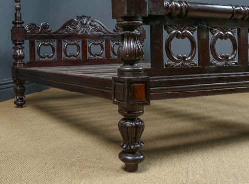 fig 7. An antique dark timber king-size four-poster bed featuring spiral turned posts, a carved footboard with circular cut-out details, and an upper canopy frame.