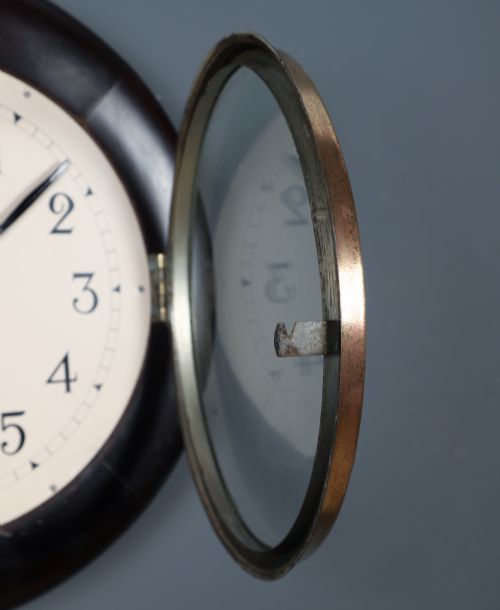 fig 2. A circular antique dark mahogany wall clock featuring a white dial with black Arabic numerals and a brass bezel.