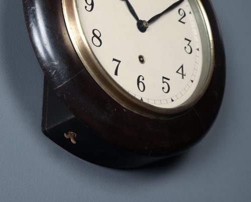 fig 5. A circular antique dark mahogany wall clock featuring a white dial with black Arabic numerals and a brass bezel.