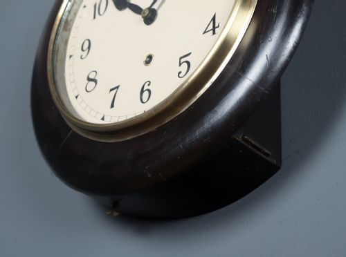 fig 6. A circular antique dark mahogany wall clock featuring a white dial with black Arabic numerals and a brass bezel.