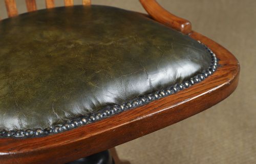 fig 4. A George V period golden oak revolving desk chair featuring a curved spindle backrest, quadruped base, and a padded green leather seat secured with brass studs.