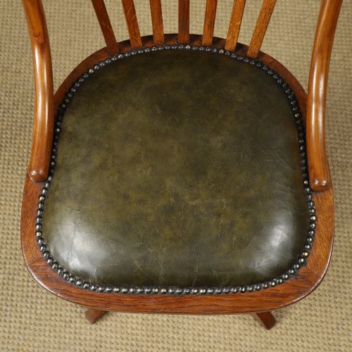 fig 5. A George V period golden oak revolving desk chair featuring a curved spindle backrest, quadruped base, and a padded green leather seat secured with brass studs.