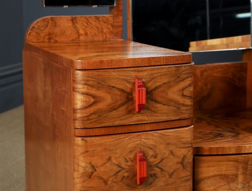 fig 3. An Art Deco figured walnut dressing table featuring twin pedestal drawers, a central curved drawer, red handles, and a three-panel upright mirror.