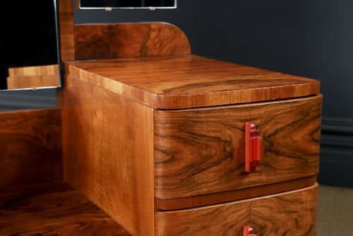 fig 5. An Art Deco figured walnut dressing table featuring twin pedestal drawers, a central curved drawer, red handles, and a three-panel upright mirror.