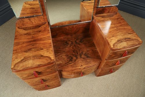 fig 6. An Art Deco figured walnut dressing table featuring twin pedestal drawers, a central curved drawer, red handles, and a three-panel upright mirror.