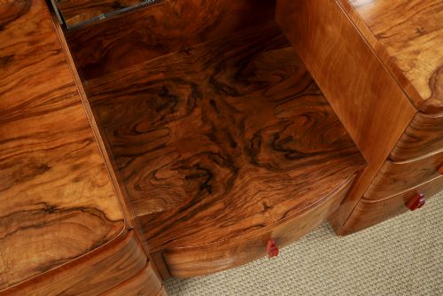 fig 7. An Art Deco figured walnut dressing table featuring twin pedestal drawers, a central curved drawer, red handles, and a three-panel upright mirror.