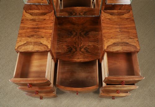 fig 9. An Art Deco figured walnut dressing table featuring twin pedestal drawers, a central curved drawer, red handles, and a three-panel upright mirror.